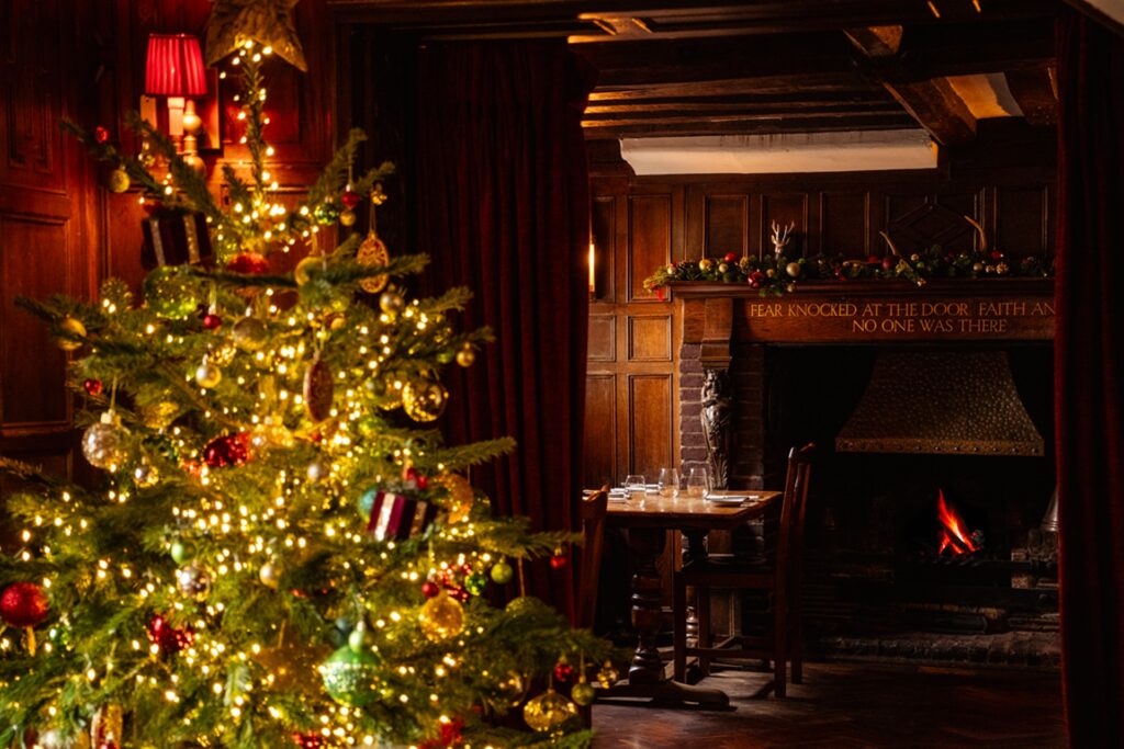 Christmas tree decorated with lights and baubles beside a lit fireplace inside The Hind’s Head in Bray.