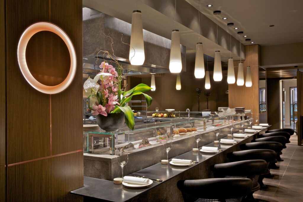 The counter at Chai Wu, with black leather stools, glass display cases and softly lit pendant lamps overlooking the open kitchen.