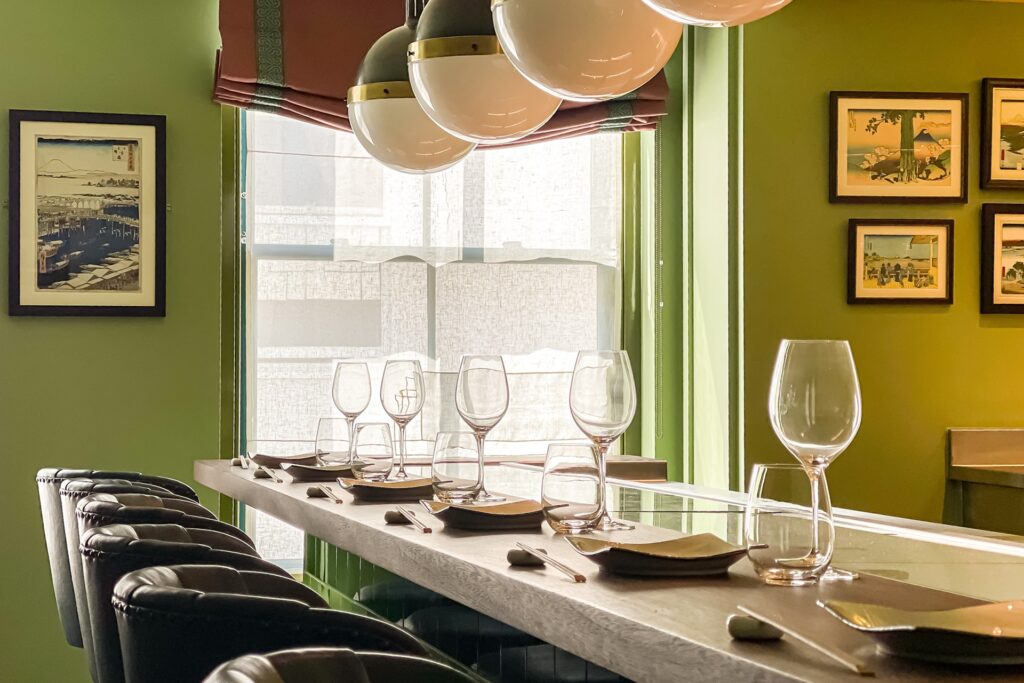 The counter at The Fuji Grill Sushi Bar at Beaverbrook Town House, with leather stools, neatly set place settings and soft natural light.