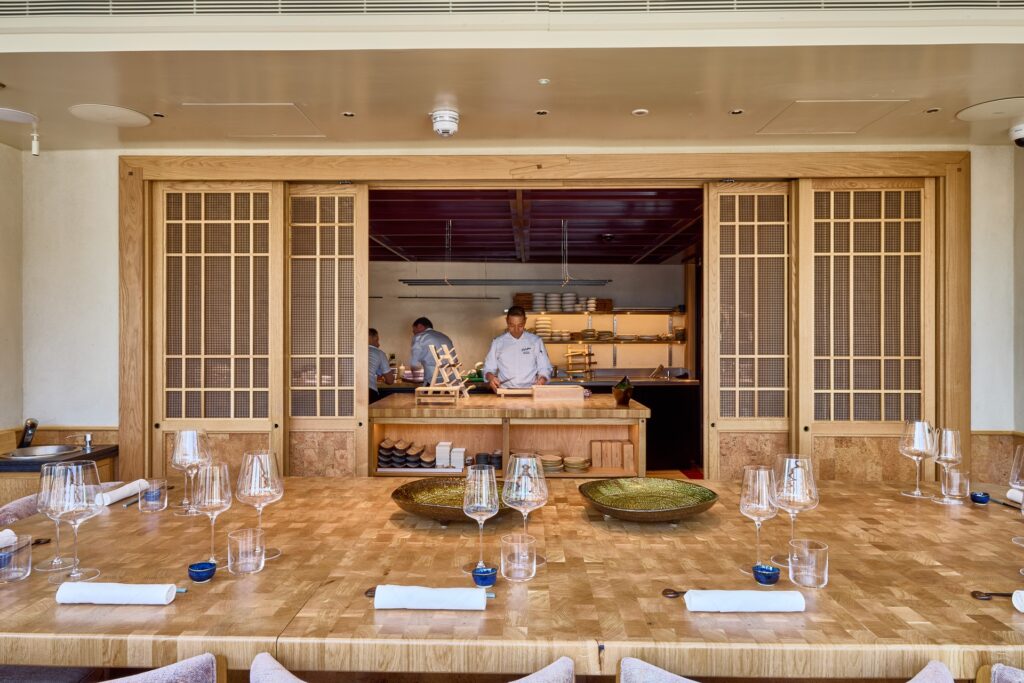 A wood-lined counter facing an open kitchen at Kioku by Endo, with chefs preparing dishes behind sliding timber screens.