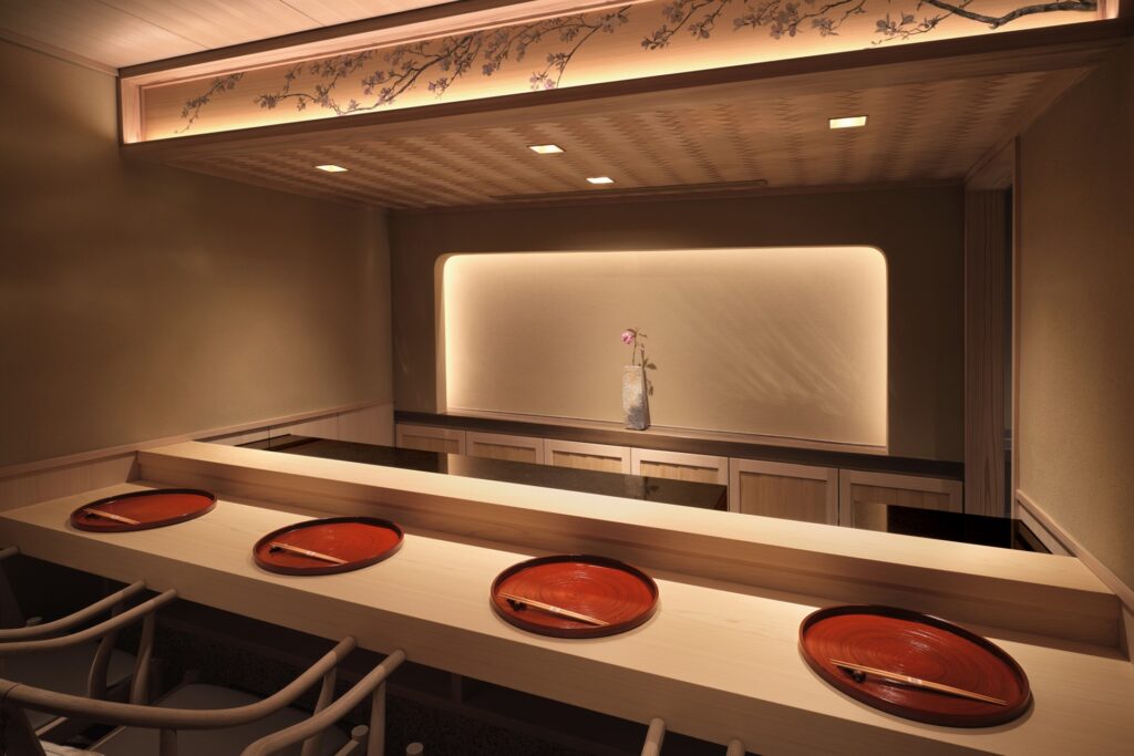 The minimalist counter at Sushi Kanesaka, with pale wood surfaces, lacquered plates and chopsticks set in a softly lit dining room.